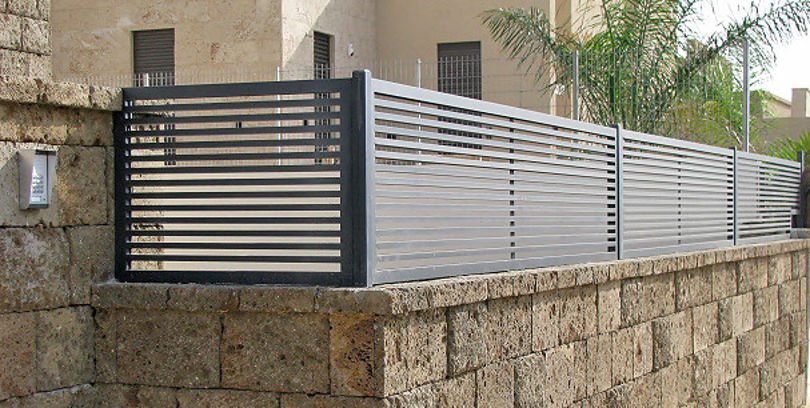 גדר אלומיניום עם רפפות אופקיות במסגרת כהה על קיר אבן