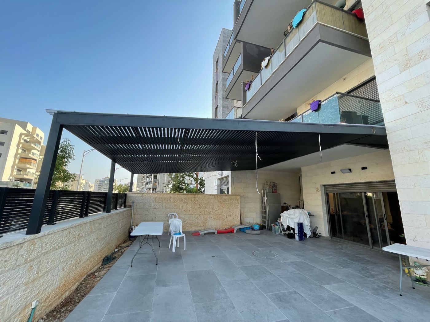 חצר רחבה מקורה בפרגולת אלומיניום כהה בחריש