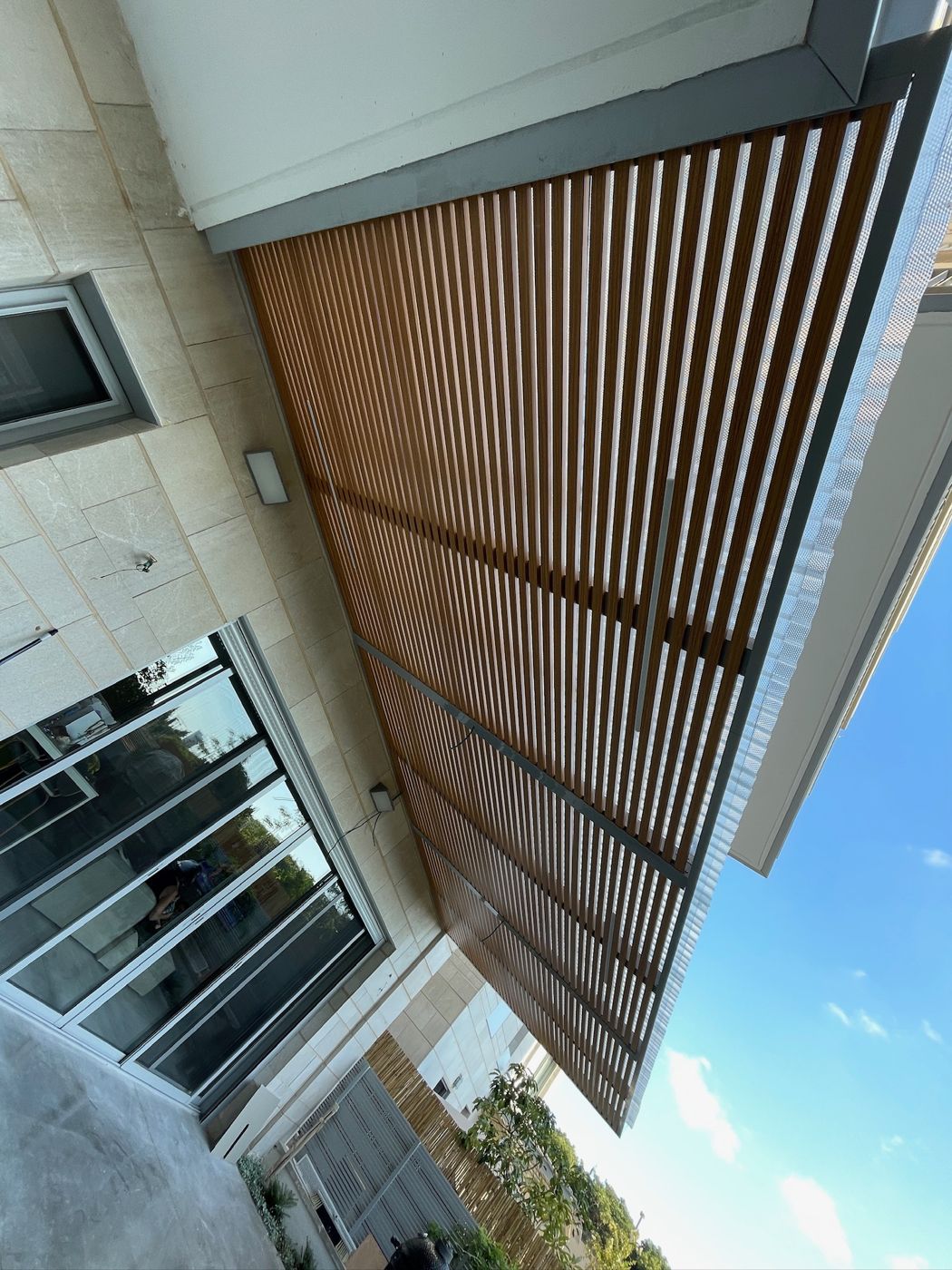 רפפות אלומיניום בגוון עץ לצד חלון בבית בהרצליה