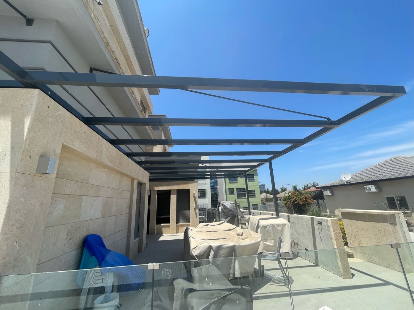 פרגולת אלומיניום כהה מעל מרפסת עם מעקה זכוכית בהוד השרון