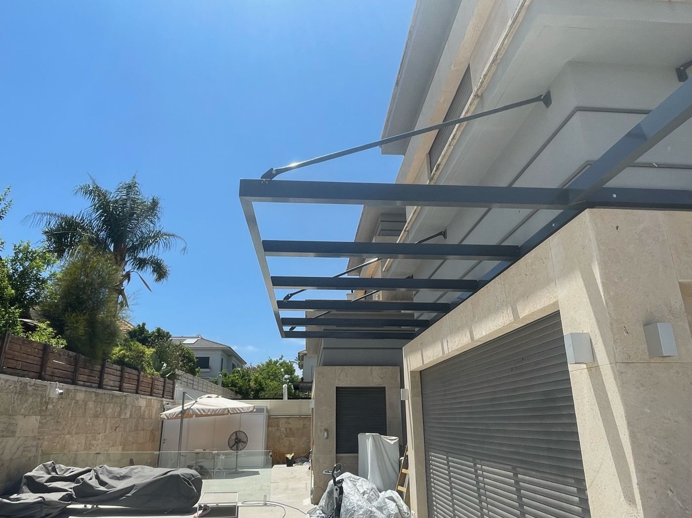 פרגולת אלומיניום כהה לצד דקל בחצר בהוד השרון