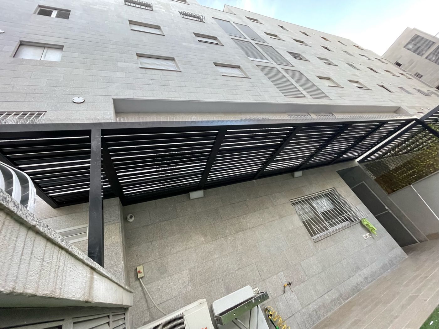 פרגולת אלומיניום כהה בחזית בניין מגורים בנתניה