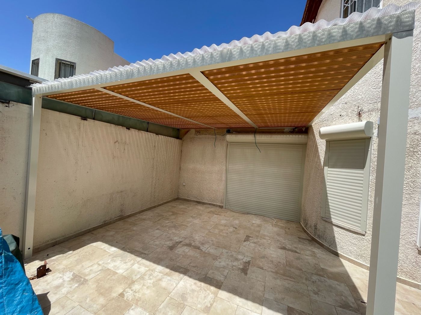 רפפות אלומיניום בגוון עץ מעל חצר מרוצפת בראש העין