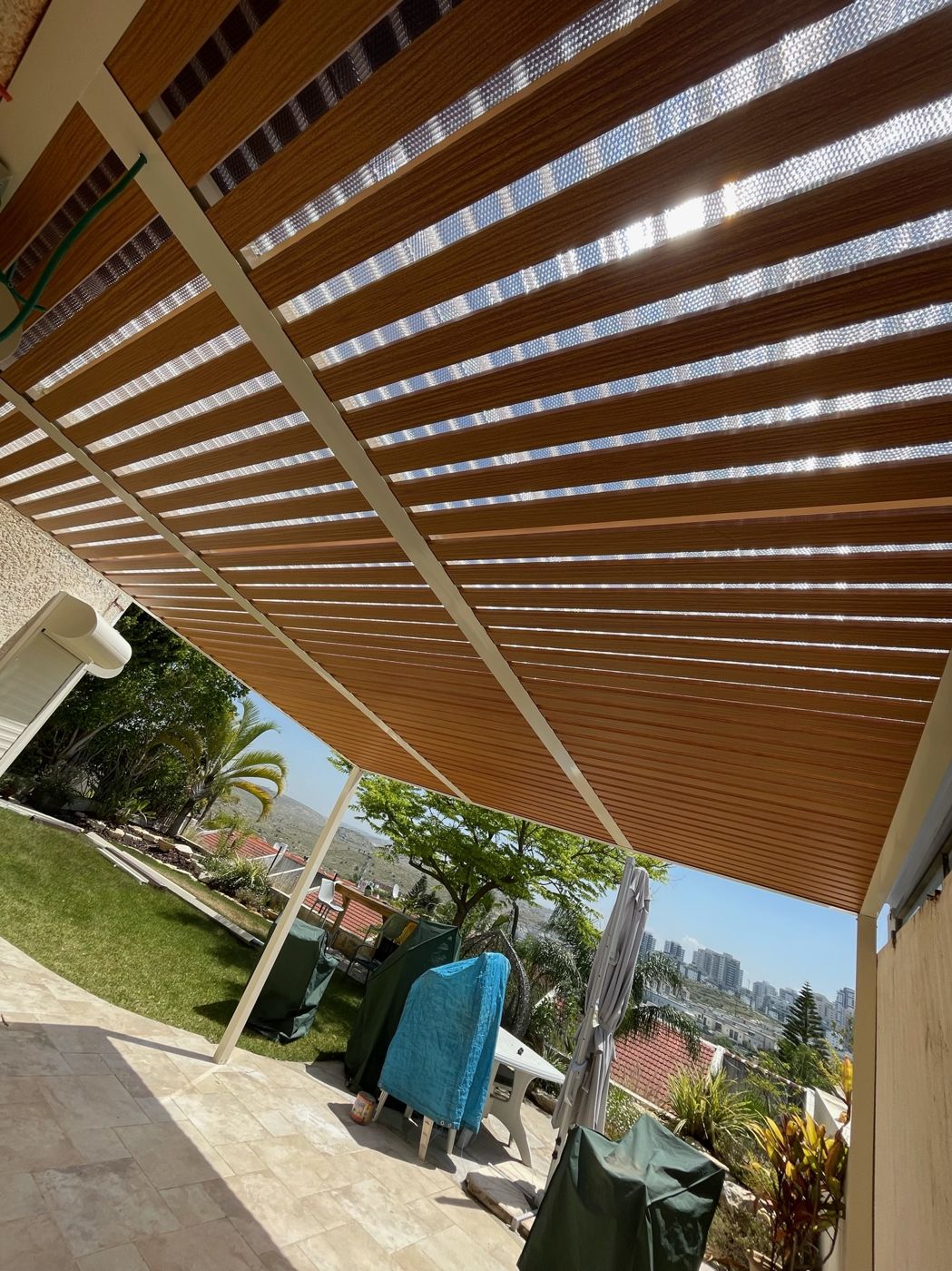 פרגולת אלומיניום עם רפפות בגוון עץ ונוף דקלים בראש העין