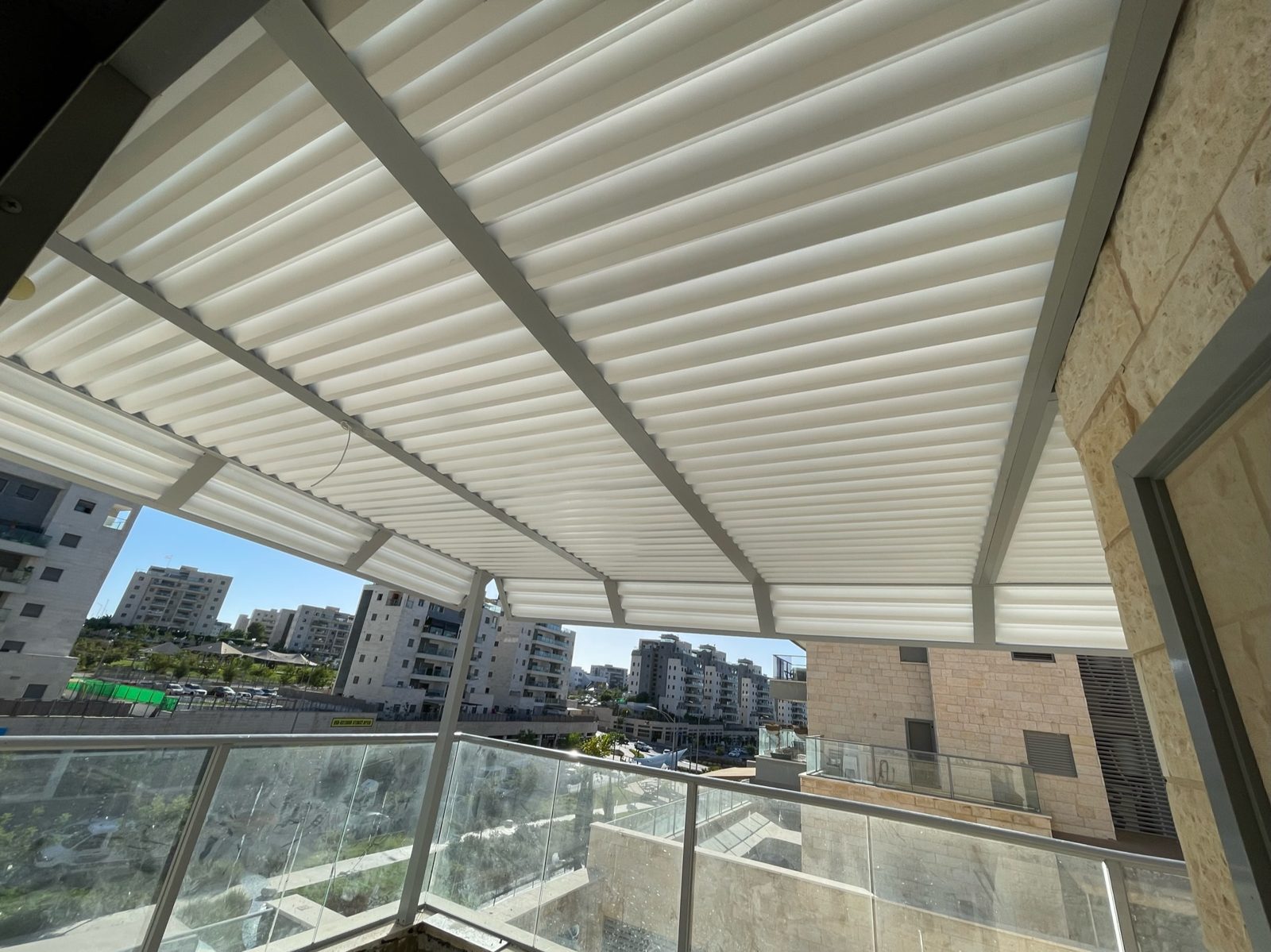 פרגולת אלומיניום בהירה מעל מרפסת דירה עם נוף העיר בחריש