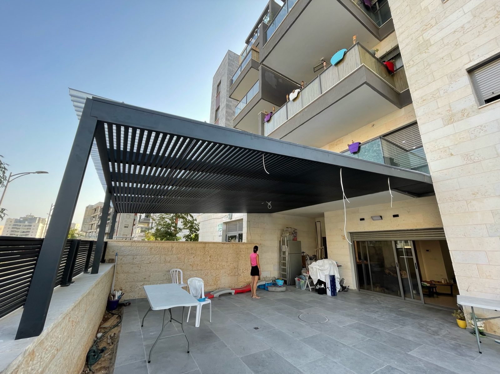 פרגולת אלומיניום כהה מעל חצר בבניין חדש בחריש