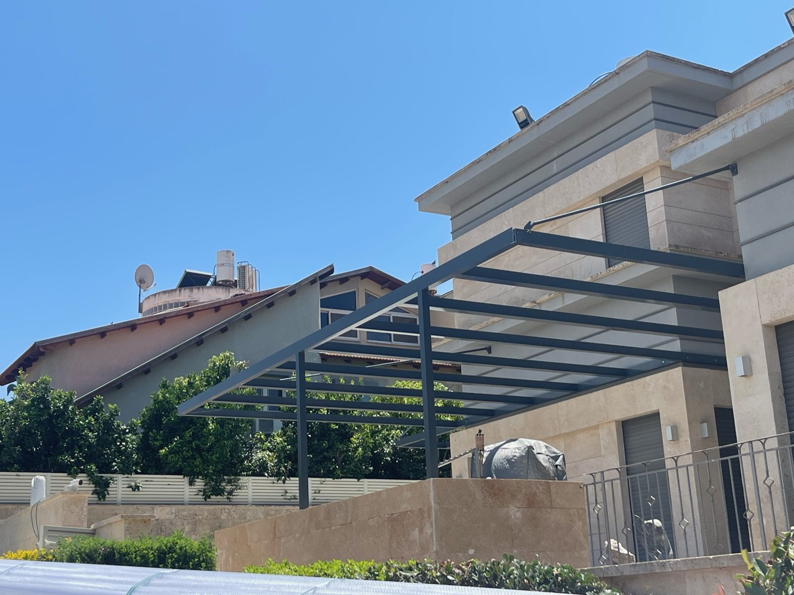 פרגולת אלומיניום כהה מעל מרפסת בבית מחופה אבן בהוד השרון