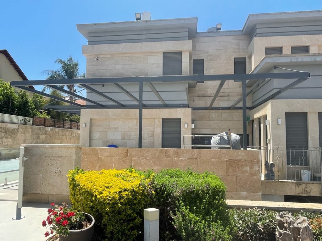 פרגולת אלומיניום כהה בווילה מחופה אבן עם גינה בהוד השרון