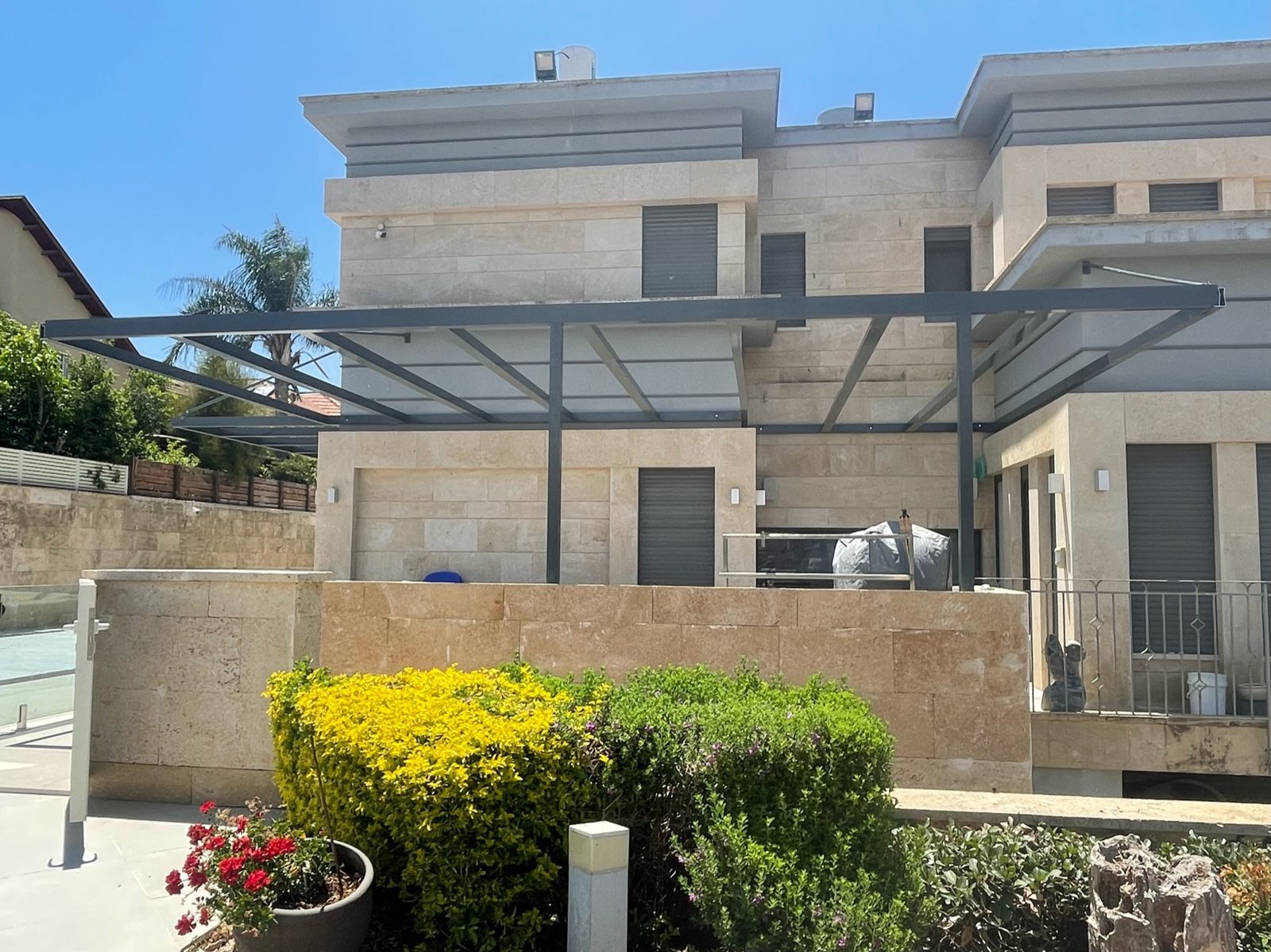 פרגולת אלומיניום כהה בווילה מחופה אבן עם גינה בהוד השרון