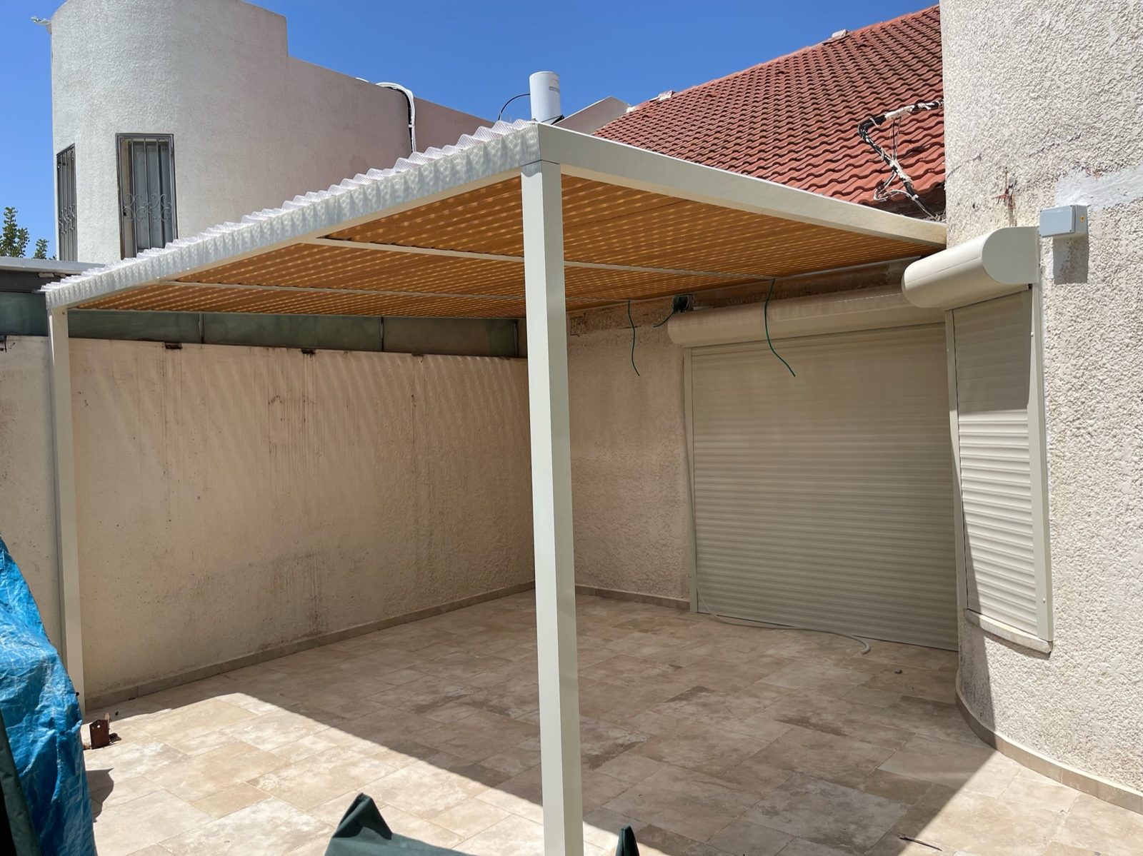 פרגולת אלומיניום עם מסגרת לבנה ורפפות בגוון עץ בחצר בראש העין