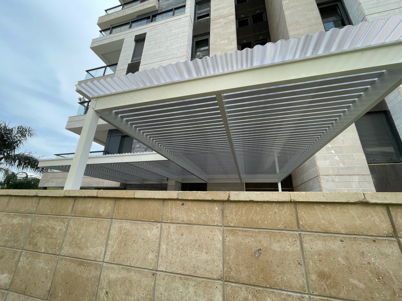 פרגולה מאלומיניום על עמודים בחצר דירת גן מול מגדל מגורים בגני תקווה
